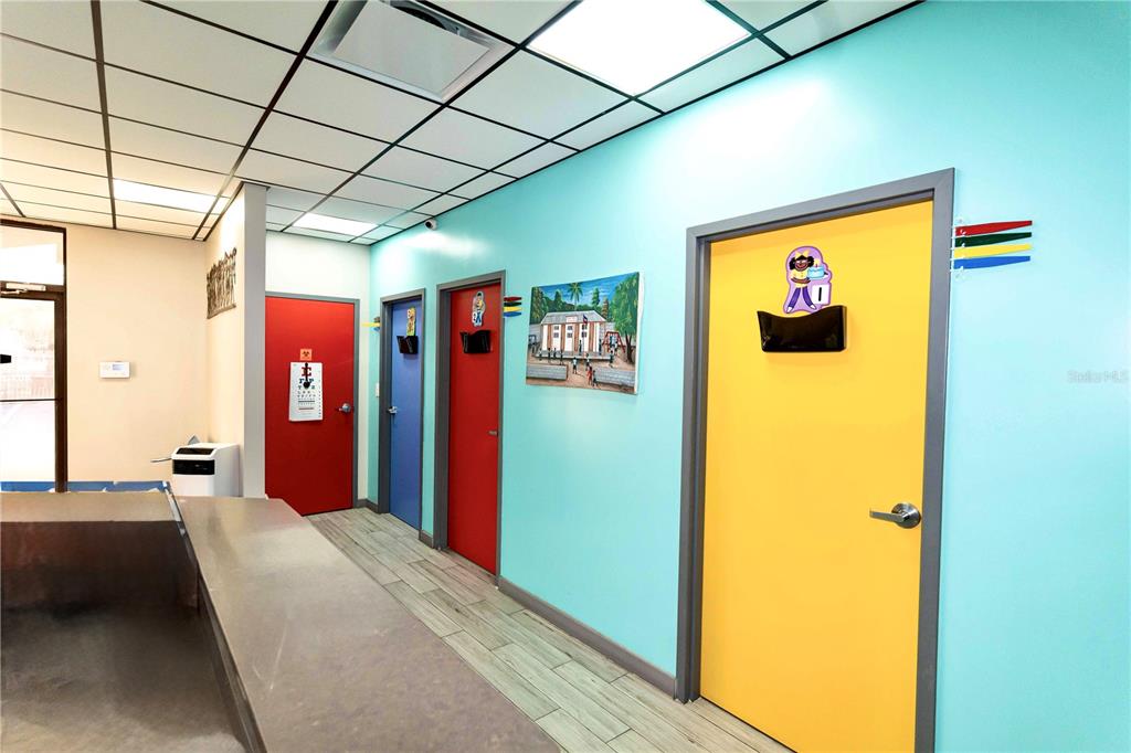 A hallway with light blue walls features four colorful doors and a drop ceiling — 4804 EDGEWATER DRIVE, ORLANDO, FL
