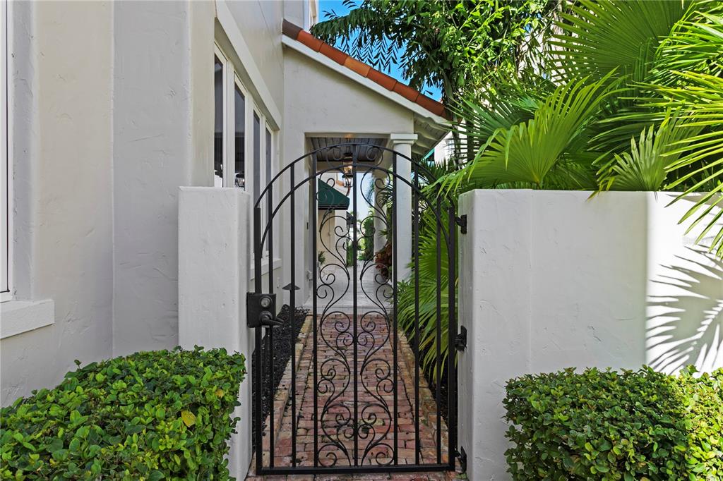 A black wrought iron gate leads to a brick walkway beside a stucco house — 1109 ABBEYS WAY, TAMPA, FL