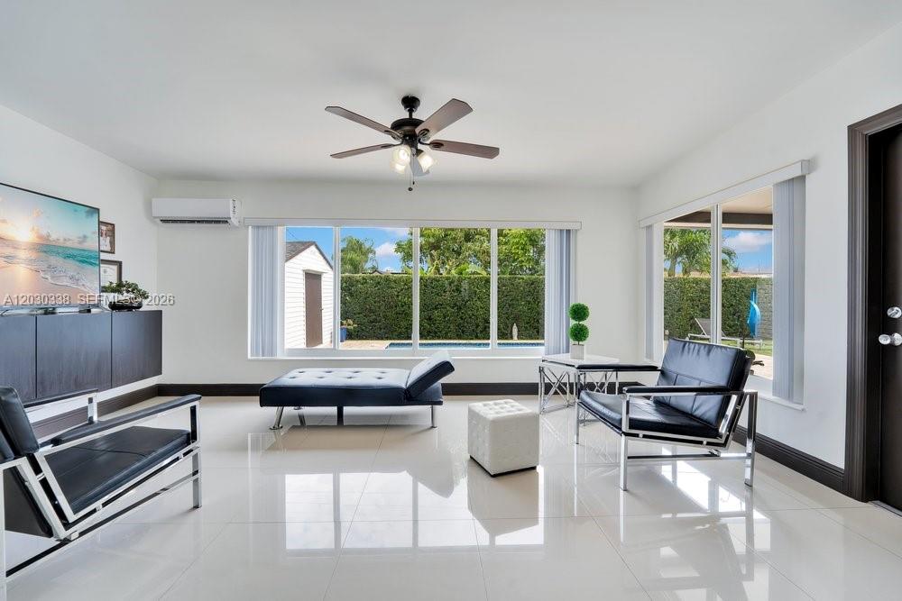 A bright living room features white tile floors, black leather furniture, and a large window — 8625 SW 44th St, Miami FL 33155, MIAMI, FL