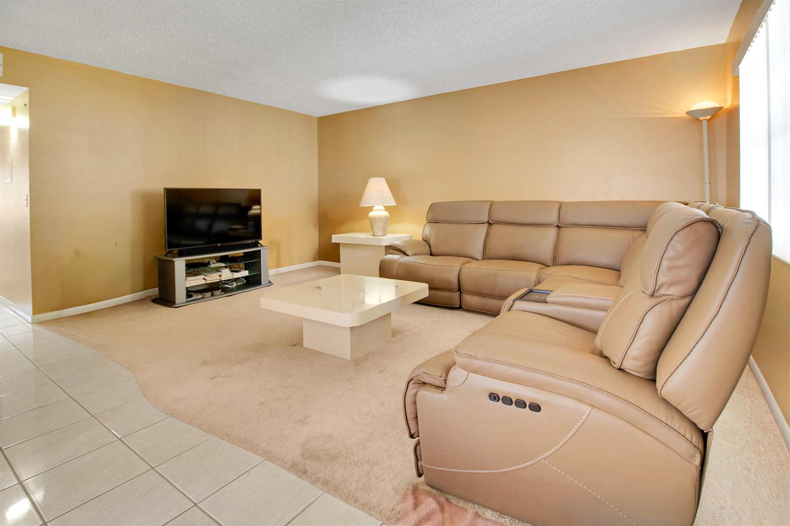 A living room features a tan sectional sofa, a coffee table, and a television console — 525 Capri K, Delray Beach FL 33484, DELRAY BEACH, FL