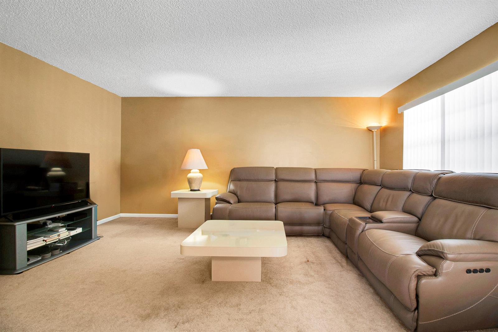 A living room features a brown sectional sofa, a coffee table, and a television stand — 525 Capri K, Delray Beach FL 33484, DELRAY BEACH, FL