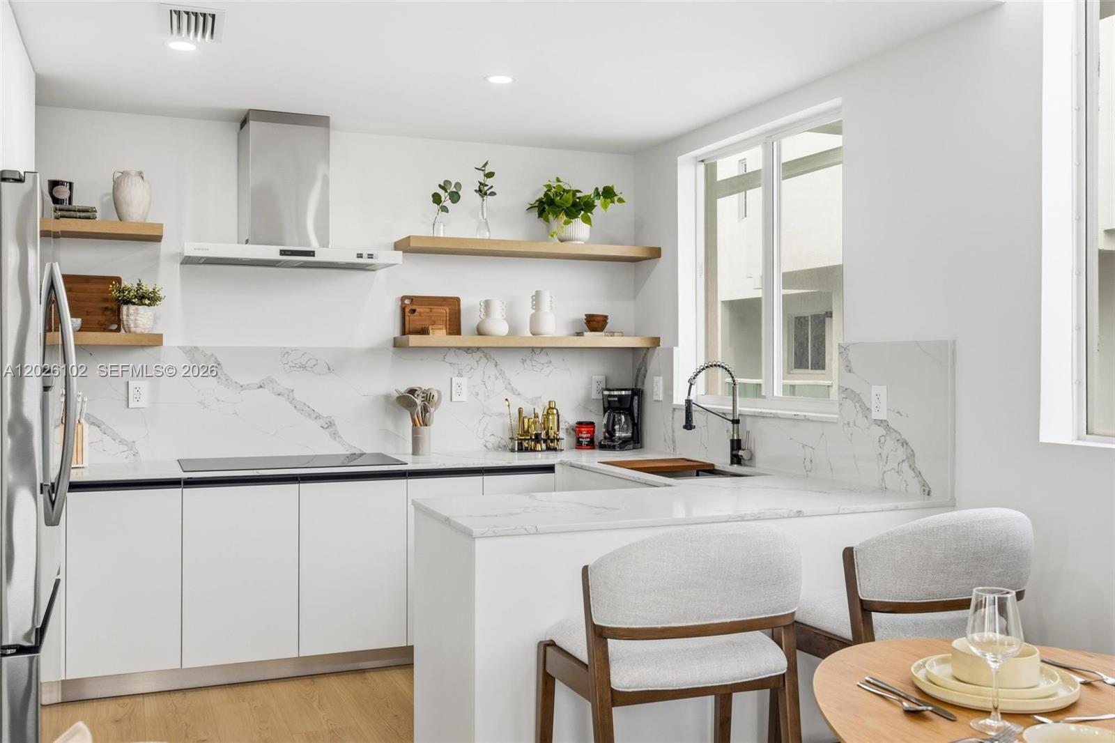 A modern kitchen features white cabinets, marble-patterned backsplashes, open wood shelving, and a breakfast bar — 1975 Calais Dr # 5, Miami Beach FL 33141, MIAMI BEACH, FL