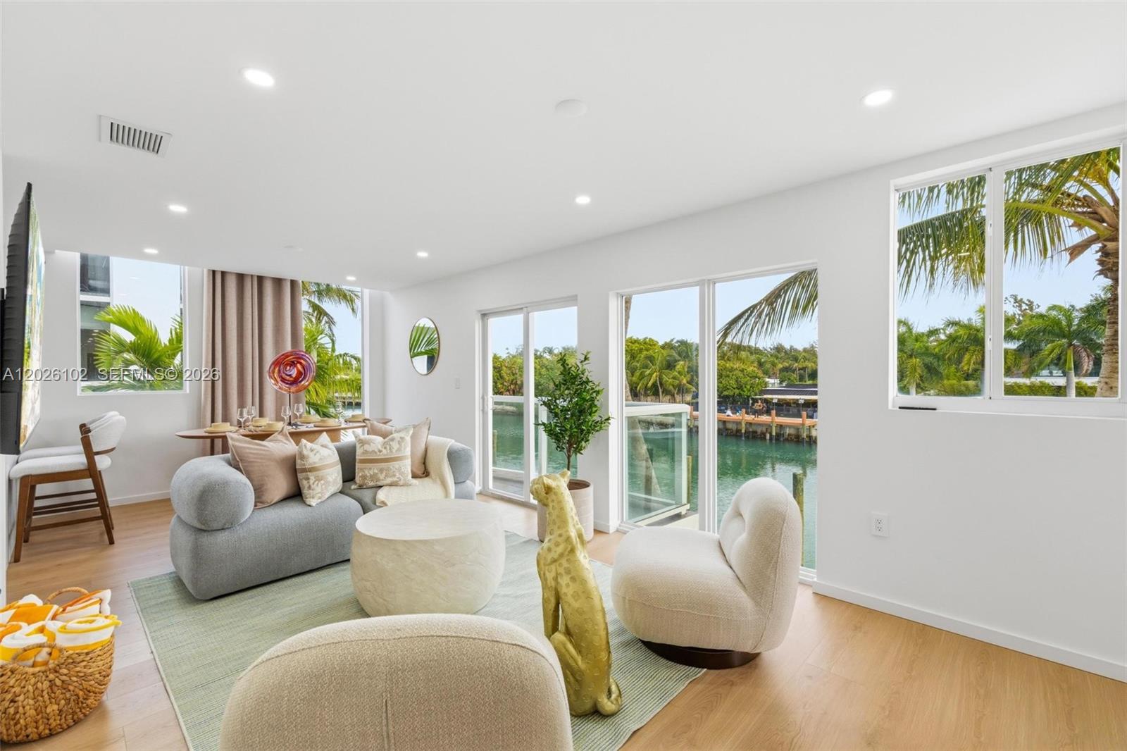 A bright living room features a gray sofa, cream chairs, and floor-to-ceiling windows overlooking water — 1975 Calais Dr # 5, Miami Beach FL 33141, MIAMI BEACH, FL