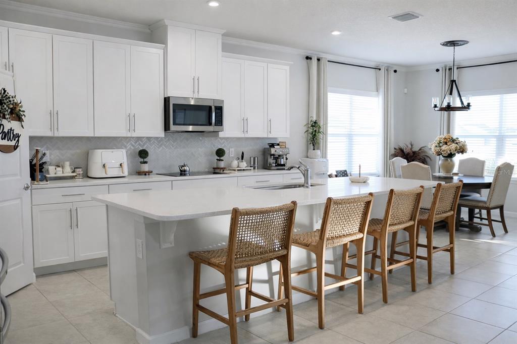 A bright kitchen features white cabinetry, a large island with woven stools, and tile flooring — 6405 PEBBLEBROOKE WAY, ZEPHYRHILLS, FL