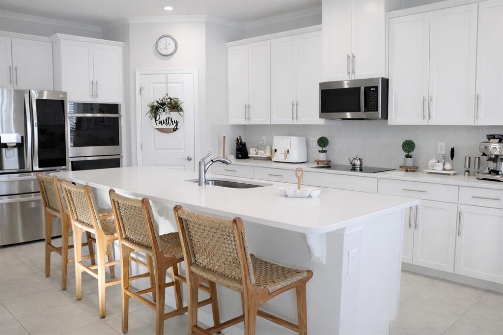 A bright kitchen features white cabinetry, a large central island with bar seating, and appliances — 6405 PEBBLEBROOKE WAY, ZEPHYRHILLS, FL