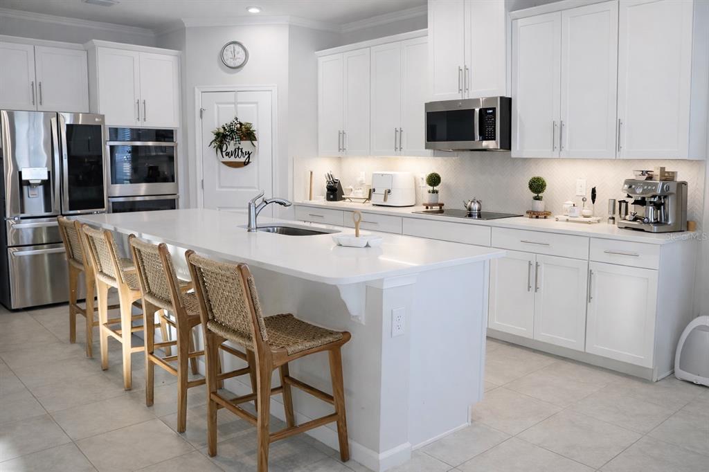 A bright kitchen features white cabinetry, a large quartz island with bar seating, and stainless appliances — 6405 PEBBLEBROOKE WAY, ZEPHYRHILLS, FL
