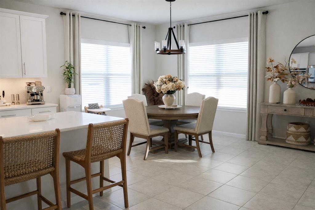 A dining area with a round wooden table, upholstered chairs, and a kitchen island nearby — 6405 PEBBLEBROOKE WAY, ZEPHYRHILLS, FL