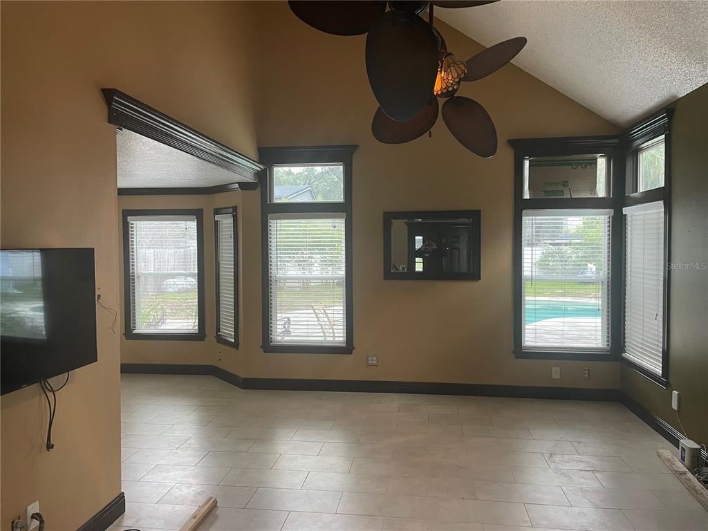 A living room with vaulted ceilings, tile floors, dark trim, and large windows overlooking a pool — 9828 BUBBLING BROOK COURT, OVIEDO, FL