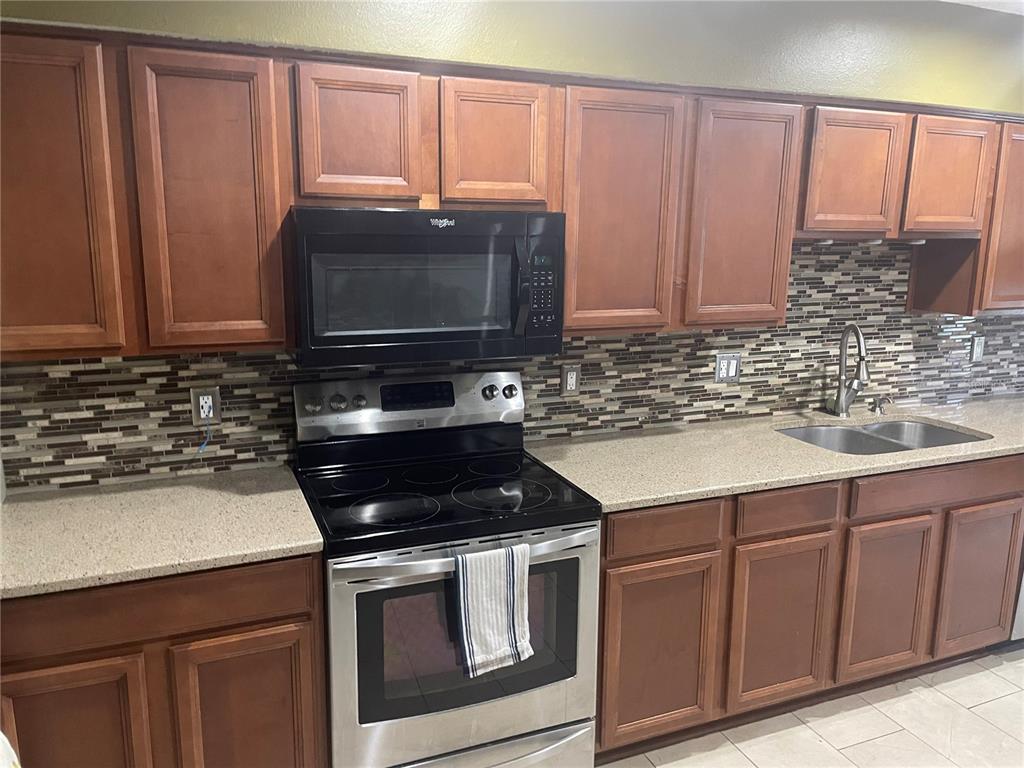 A kitchen features wood cabinets, stainless steel appliances, a tiled backsplash, and light-colored countertops — 9828 BUBBLING BROOK COURT, OVIEDO, FL