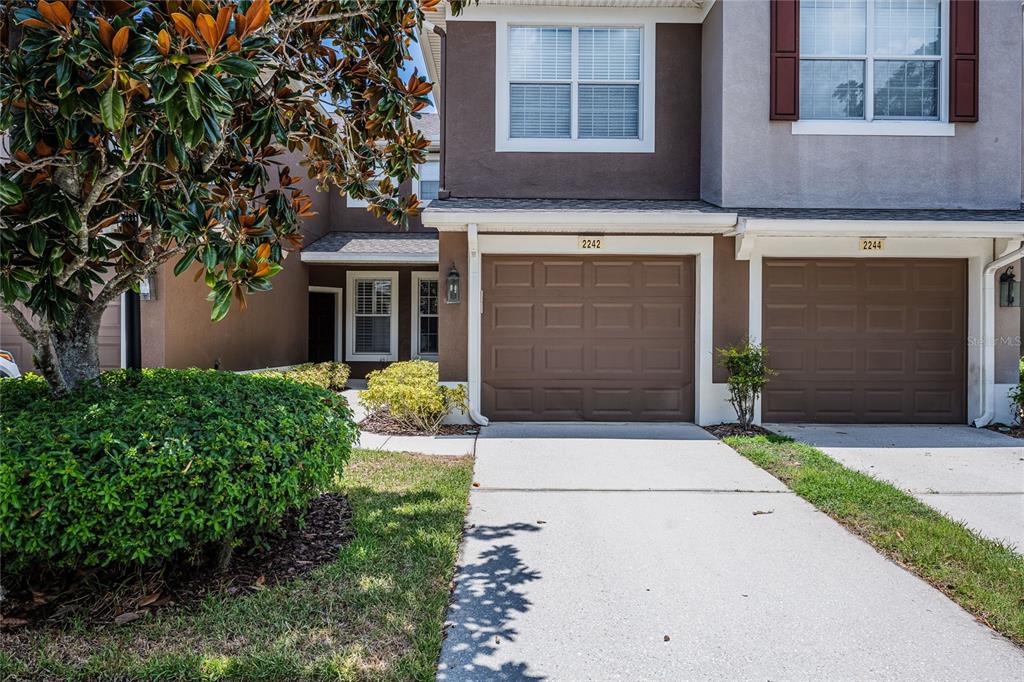 The exterior of two attached townhomes features brown garage doors and beige stucco walls — 2242 KINGS PALACE DRIVE UNIT 2242, RIVERVIEW, FL