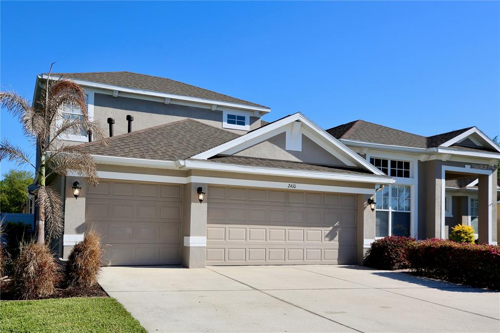 A two-story house with a beige stucco exterior and a three-car garage — 2410 TEA OLIVE TERRACE, VALRICO, FL