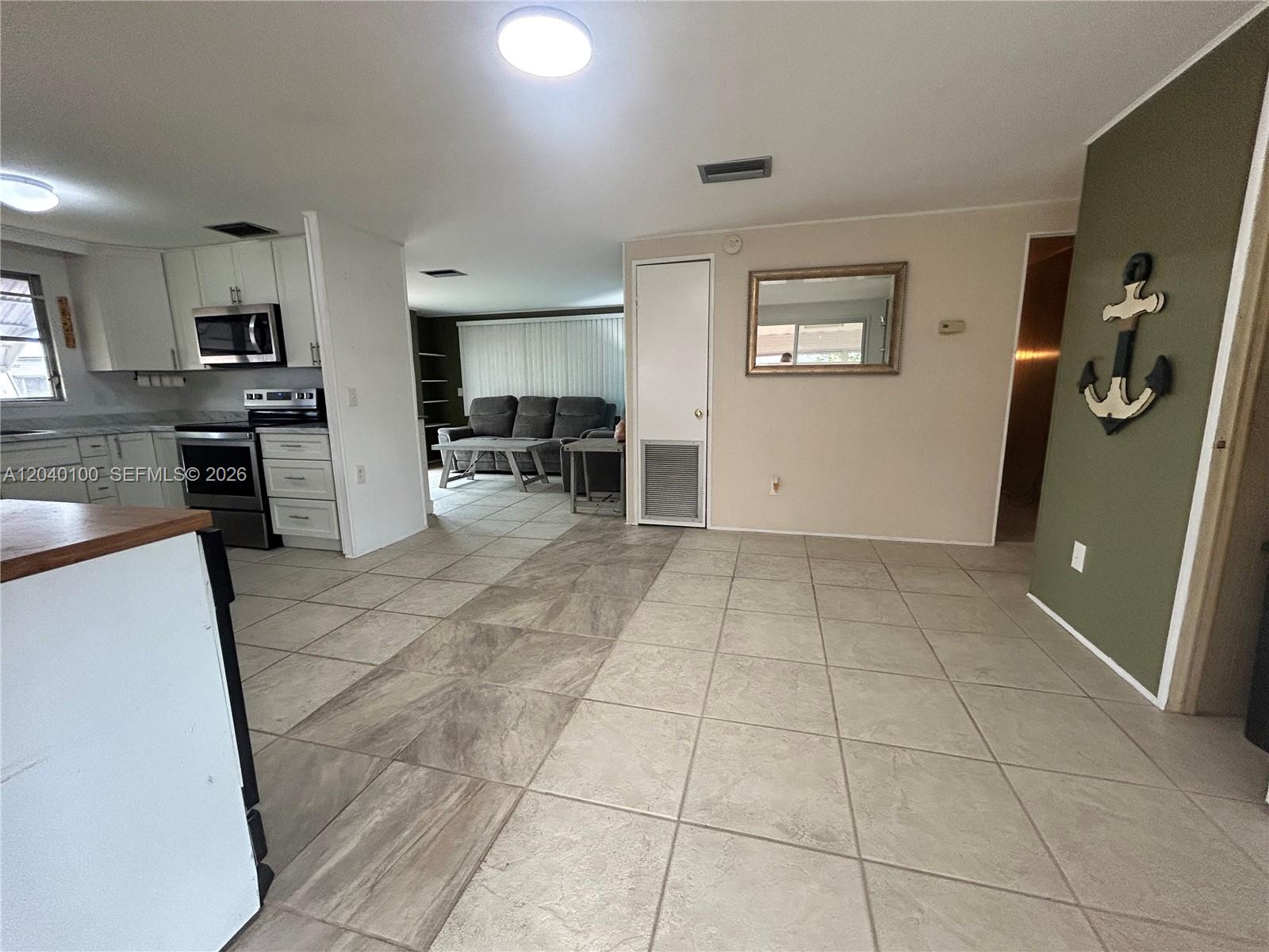 A kitchen with white cabinets and stainless appliances opens into a living area with tile — 2341 SW 84th Ave, Davie FL 33324, DAVIE, FL