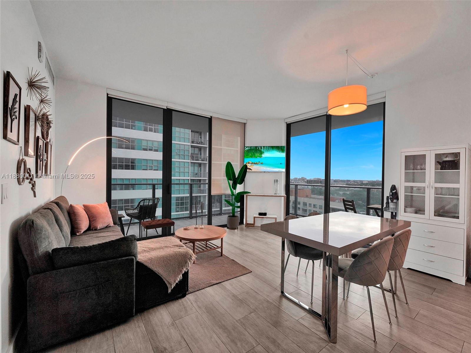 A modern living and dining area features floor-to-ceiling windows, wood-look flooring, and neutral furniture — 121 NE 34th St # 1601, Miami FL 33137, MIAMI, FL