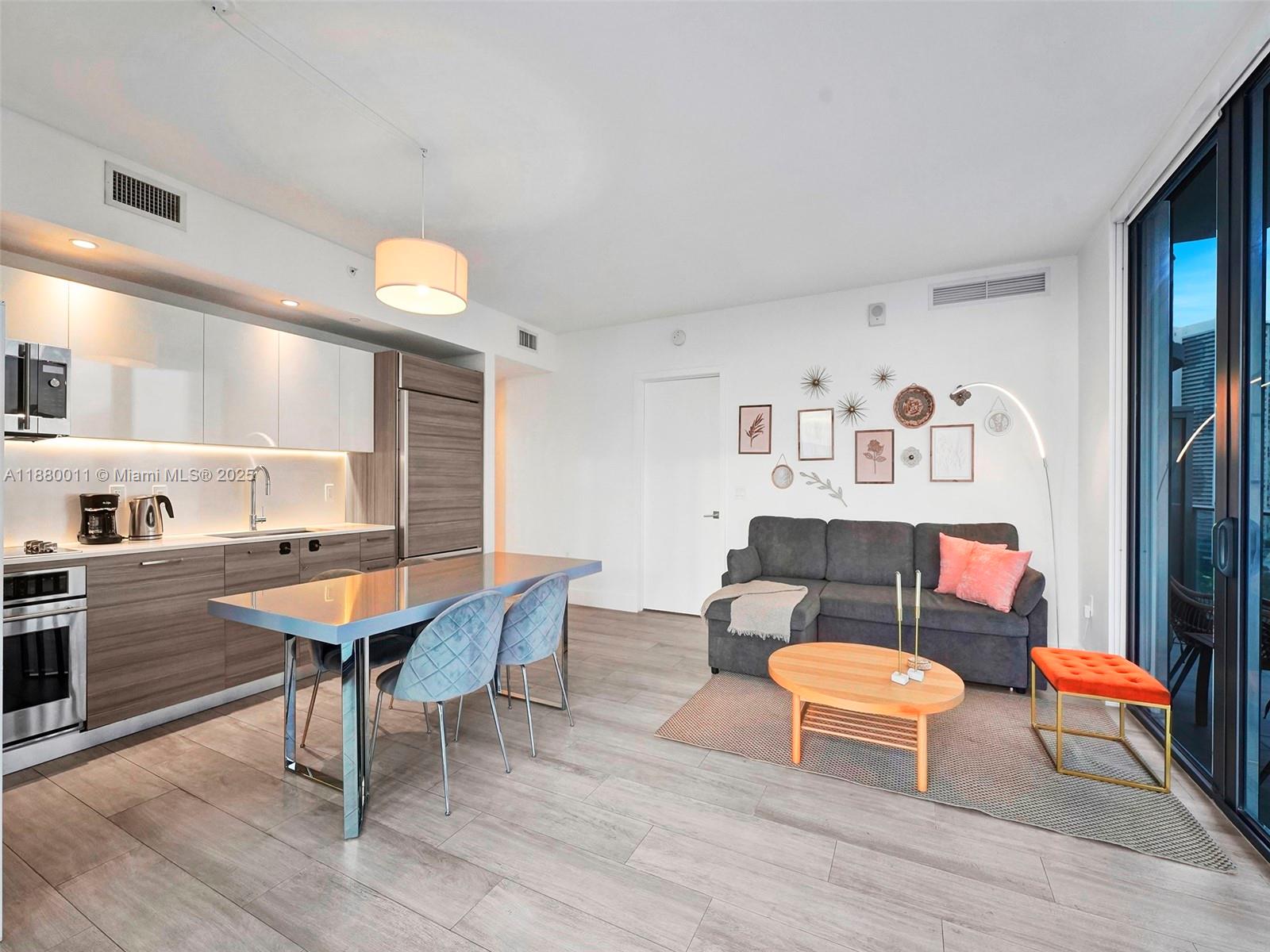 A modern open-concept living area features a kitchen with wood cabinetry and a gray sofa — 121 NE 34th St # 1601, Miami FL 33137, MIAMI, FL