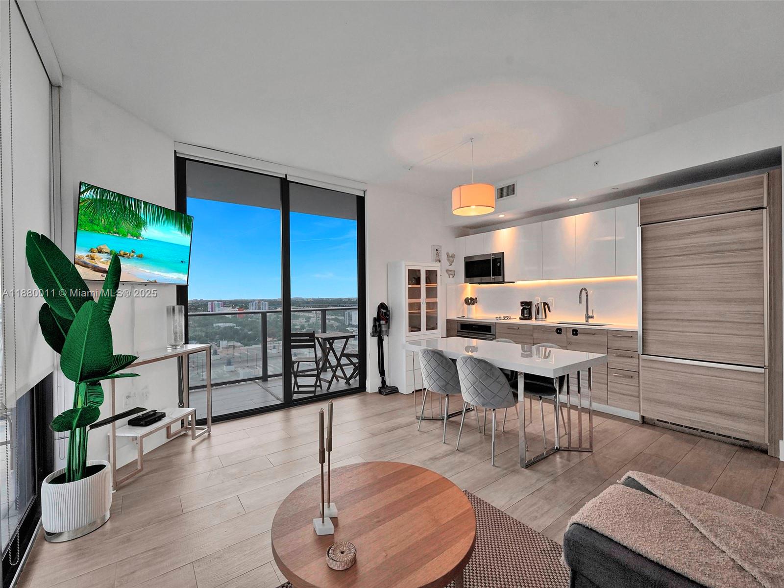 A modern apartment living area features a kitchen, dining table, and balcony with city views — 121 NE 34th St # 1601, Miami FL 33137, MIAMI, FL