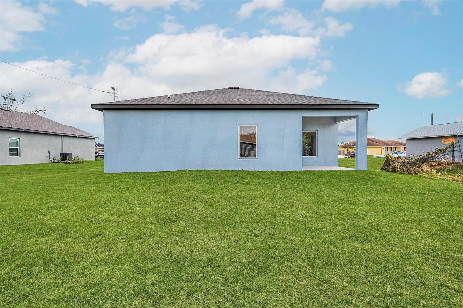 The back exterior of a light blue, single-story house with a covered patio and lawn — 7705 105th Court, Vero Beach FL 32967, VERO BEACH, FL