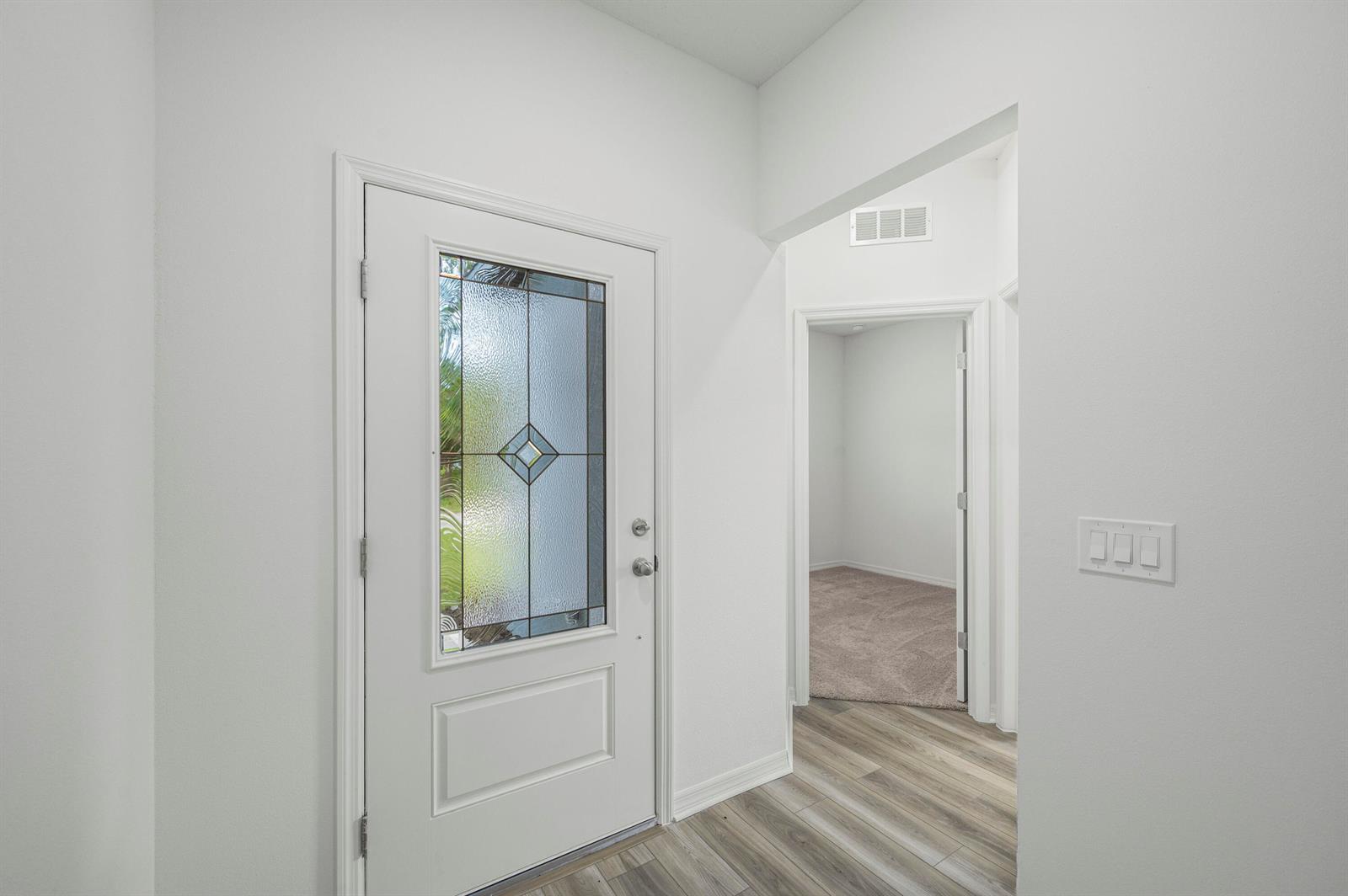 An entryway features a white front door with a decorative glass insert and wood-look flooring — 7705 105th Court, Vero Beach FL 32967, VERO BEACH, FL