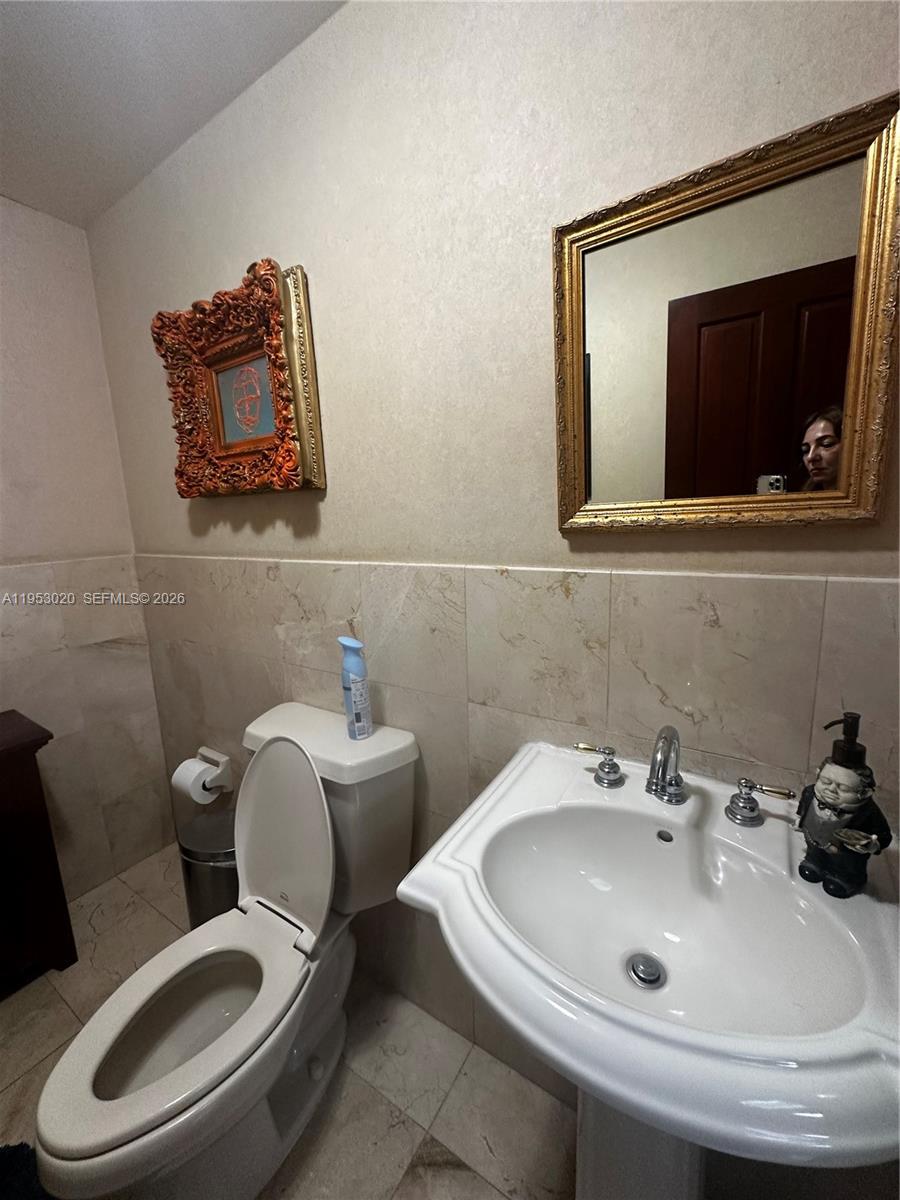 A bathroom features a pedestal sink, a toilet, a framed mirror, and decorative wall art — 1105 SW 87th Ave, Miami FL 33174, MIAMI, FL