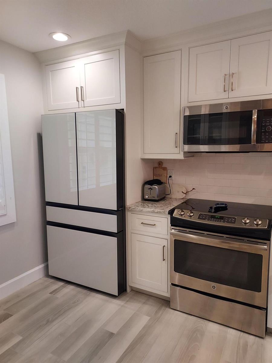A kitchen features white cabinets, a modern refrigerator, a stainless steel stove, and wood flooring — 717 S Us Hwy 1 S # 118, Jupiter FL 33477, JUPITER, FL