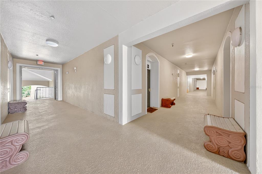 An indoor hallway with beige walls, textured flooring, and decorative benches leads to an exit — 2788 ALMATON LOOP UNIT 404, KISSIMMEE, FL