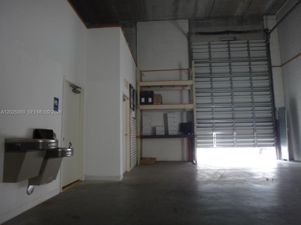 This warehouse space features a concrete floor, a roll-up door, shelving, and a water fountain — 1365 NW 98th Ct # 5, Doral FL 33172, DORAL, FL