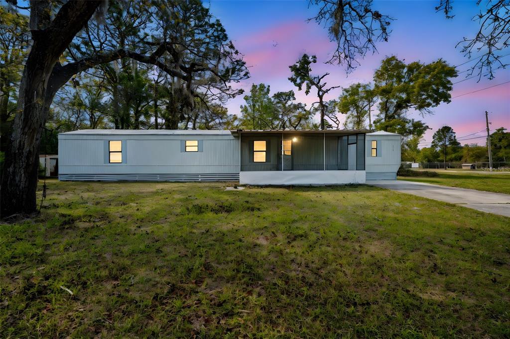 A single-story manufactured home with a screened-in porch sits on a grassy lot at dusk — 8110 W ROSELLA COURT, CRYSTAL RIVER, FL