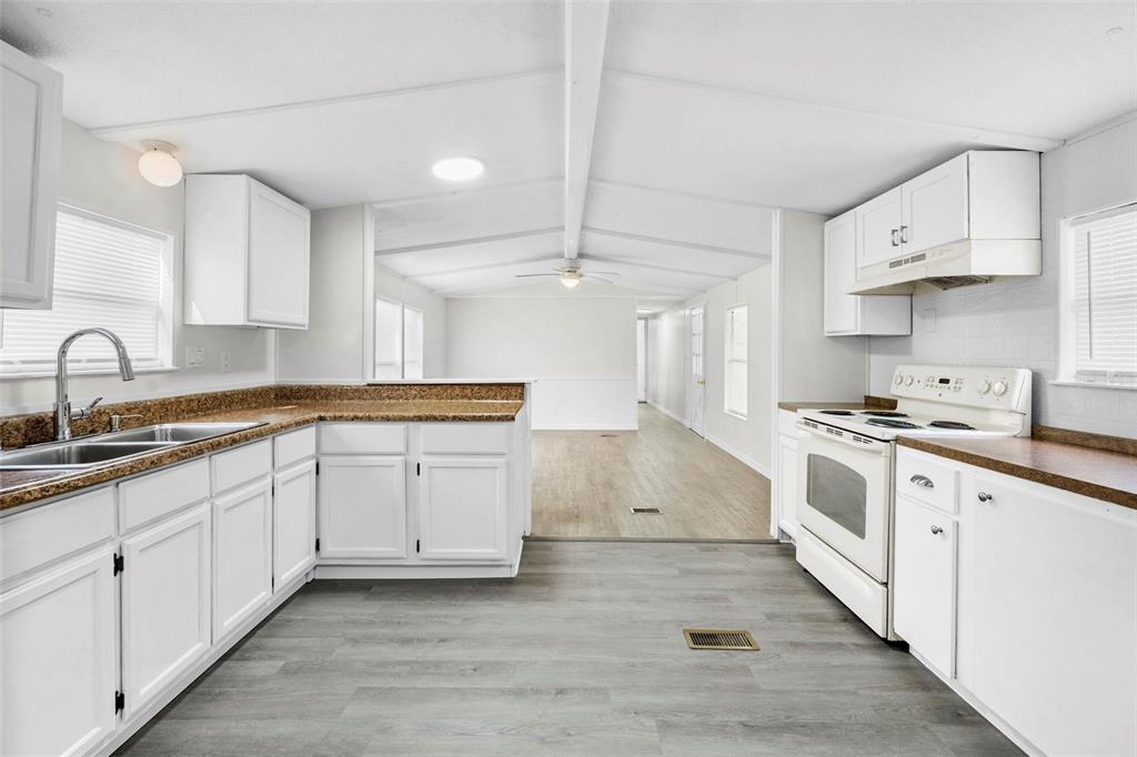 A kitchen with white cabinets, brown countertops, and light wood-look flooring opens to a hallway — 8110 W ROSELLA COURT, CRYSTAL RIVER, FL