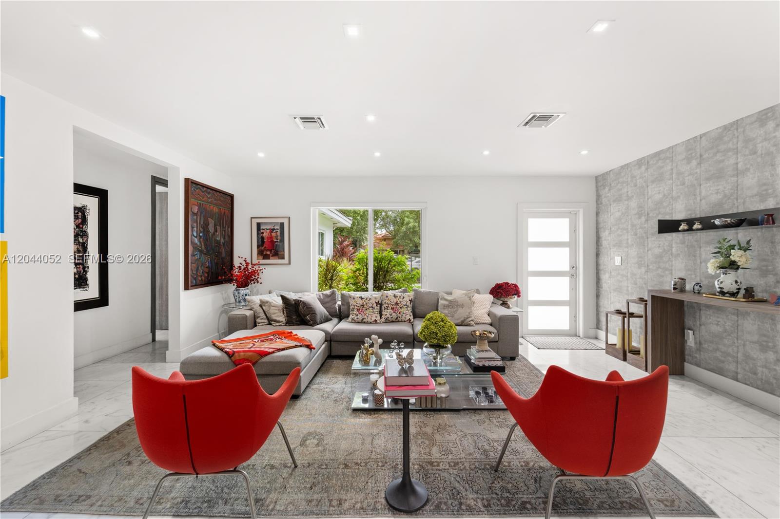 A living room features a grey sectional sofa, two red chairs, and a stone-textured wall — 721 Bird Rd, Coral Gables FL 33146, CORAL GABLES, FL