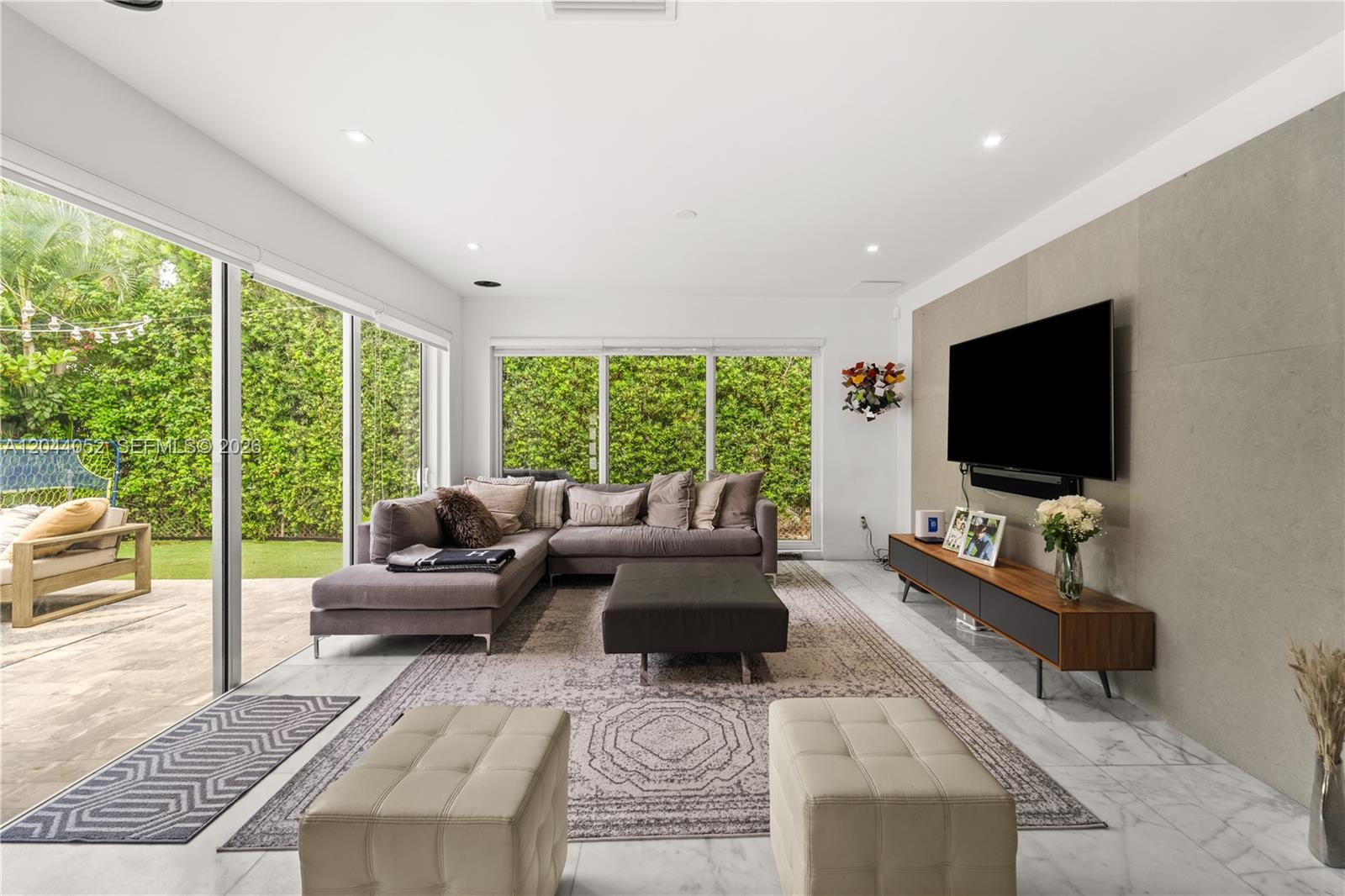 A modern living room features a sectional sofa, a wall-mounted television, and floor-to-ceiling glass doors — 721 Bird Rd, Coral Gables FL 33146, CORAL GABLES, FL