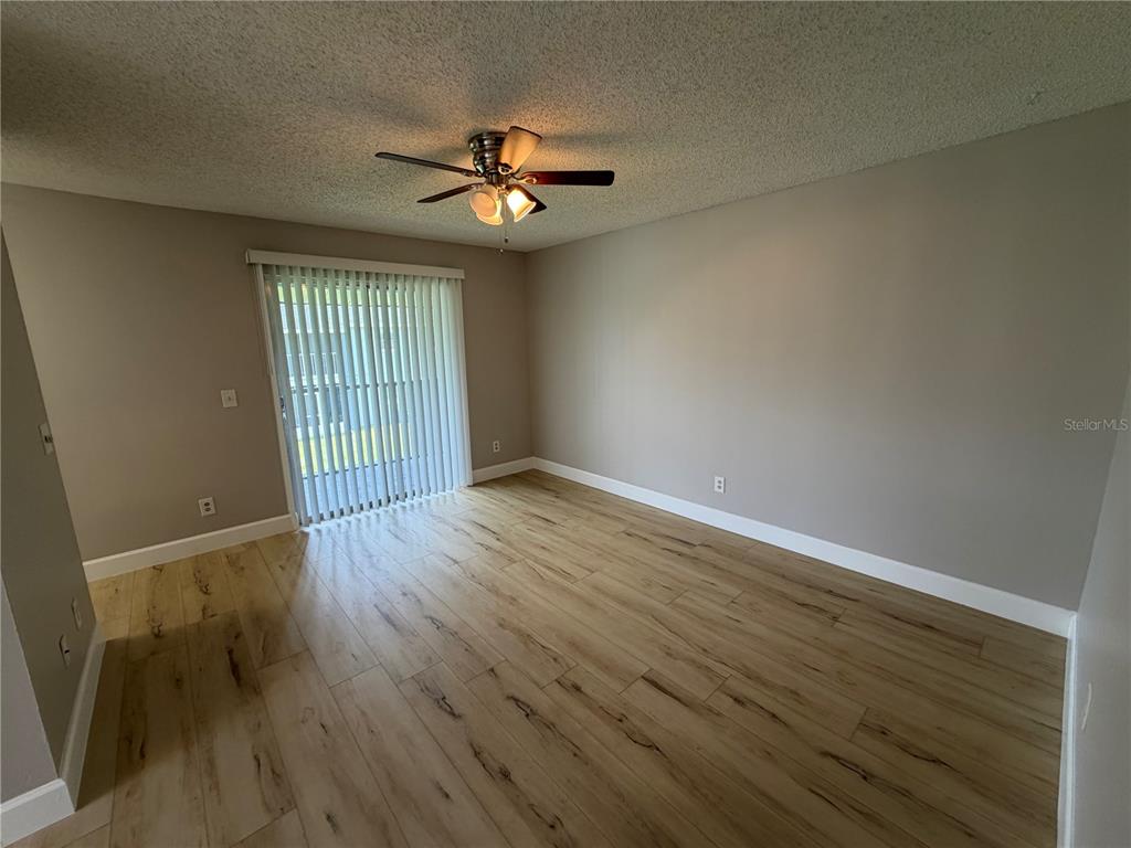 An empty room features light wood-look flooring, a ceiling fan, and sliding glass patio doors — 4160 PERSHING POINTE PLACE UNIT 3, ORLANDO, FL