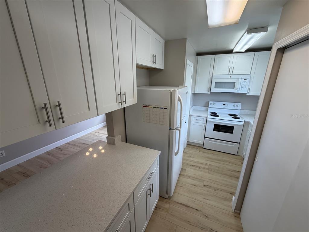 A kitchen features white cabinets, light countertops, white appliances, and wood-look flooring — 4160 PERSHING POINTE PLACE UNIT 3, ORLANDO, FL