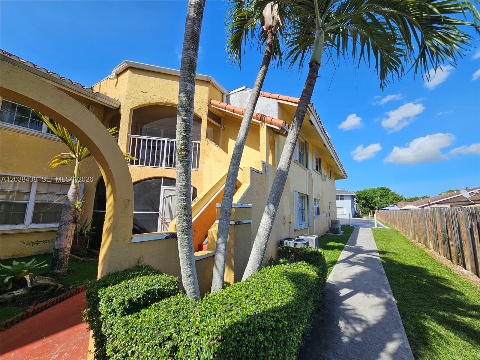 A yellow two-story building features a balcony, exterior stairs, and palm trees along a walkway — 15665 SW 74th Cir Dr # 12, Miami FL 33193, MIAMI, FL