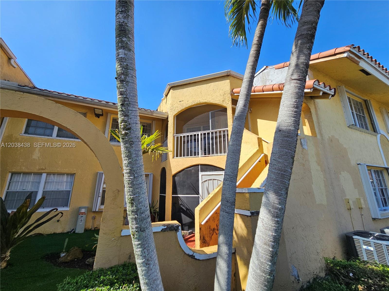A yellow two-story building features a screened balcony, arched entryway, and palm trees in front — 15665 SW 74th Cir Dr # 12, Miami FL 33193, MIAMI, FL