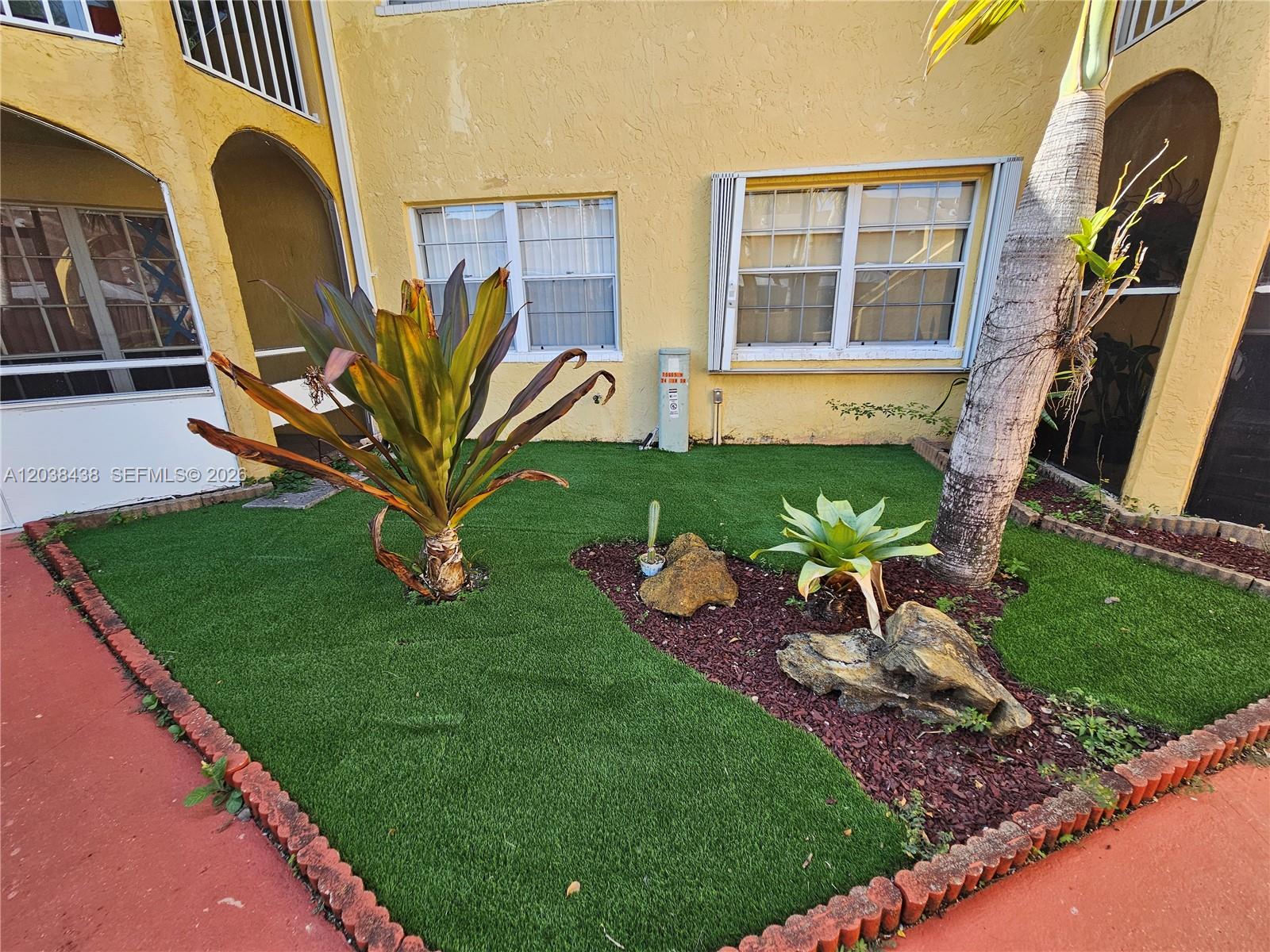 A small courtyard features artificial turf, a palm tree, decorative rocks, and tropical plants — 15665 SW 74th Cir Dr # 12, Miami FL 33193, MIAMI, FL