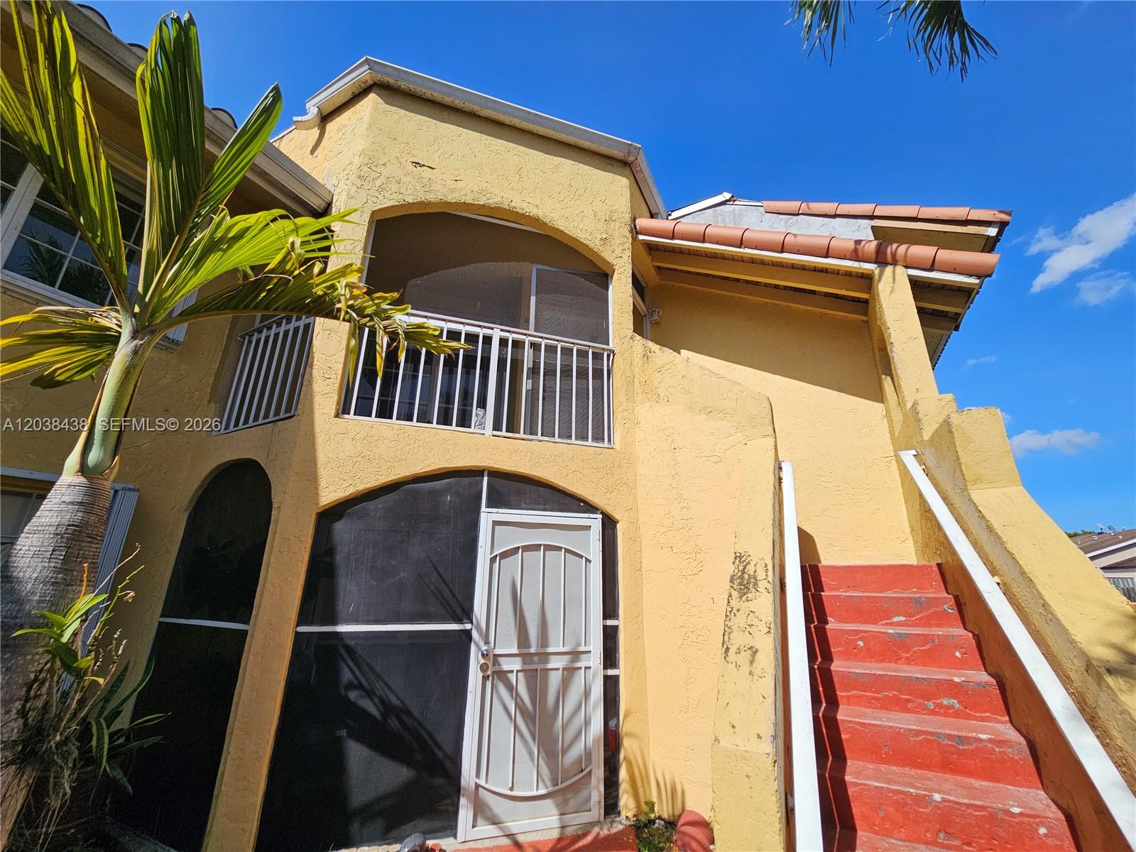 A yellow two-story building features a screened balcony, a white security door, and red stairs — 15665 SW 74th Cir Dr # 12, Miami FL 33193, MIAMI, FL
