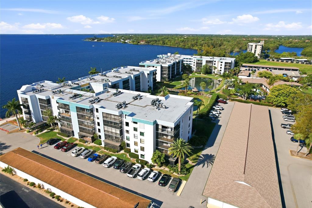 An aerial view shows multi-story apartment buildings situated along a lake with parking lots — 3460 N KEY DRIVE UNIT 407, NORTH FORT MYERS, FL