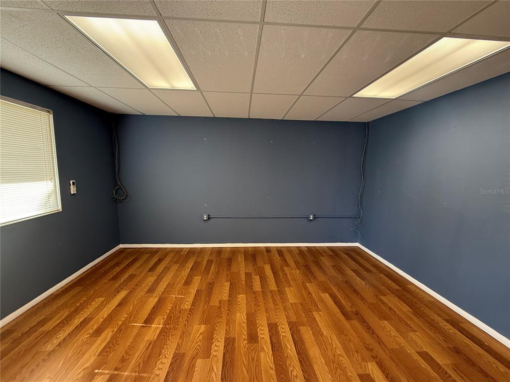 An empty room features dark blue walls, wood-look flooring, and a drop ceiling with lights — 2755 VISTA PARKWAY UNIT I-2, WEST PALM BEACH, FL