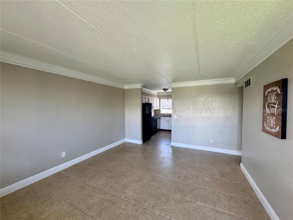 An open living area with beige walls, tile flooring, and a view into the kitchen — 1400 EUDORA ROAD UNIT D36, MOUNT DORA, FL