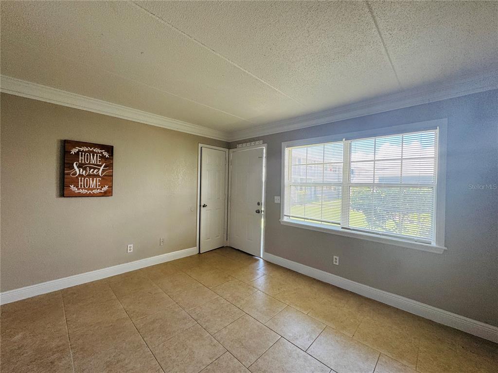 An empty room with beige walls, tile flooring, a window with blinds, and two doors — 1400 EUDORA ROAD UNIT D36, MOUNT DORA, FL