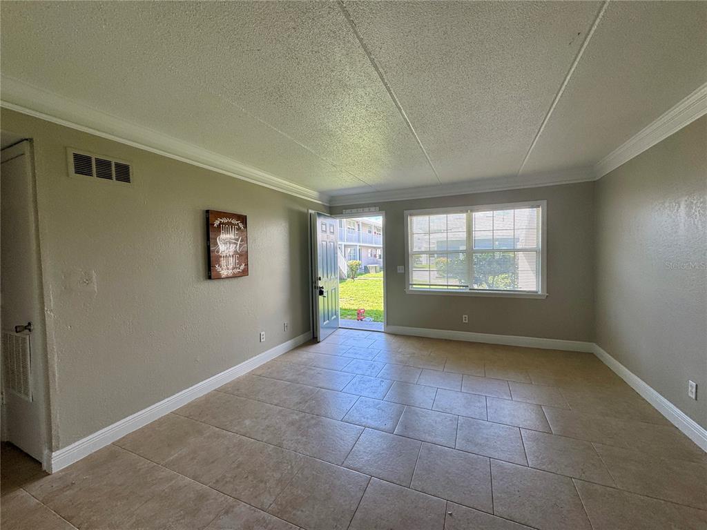 An empty living room features beige tile flooring, light-colored walls, and an open exterior door — 1400 EUDORA ROAD UNIT D36, MOUNT DORA, FL