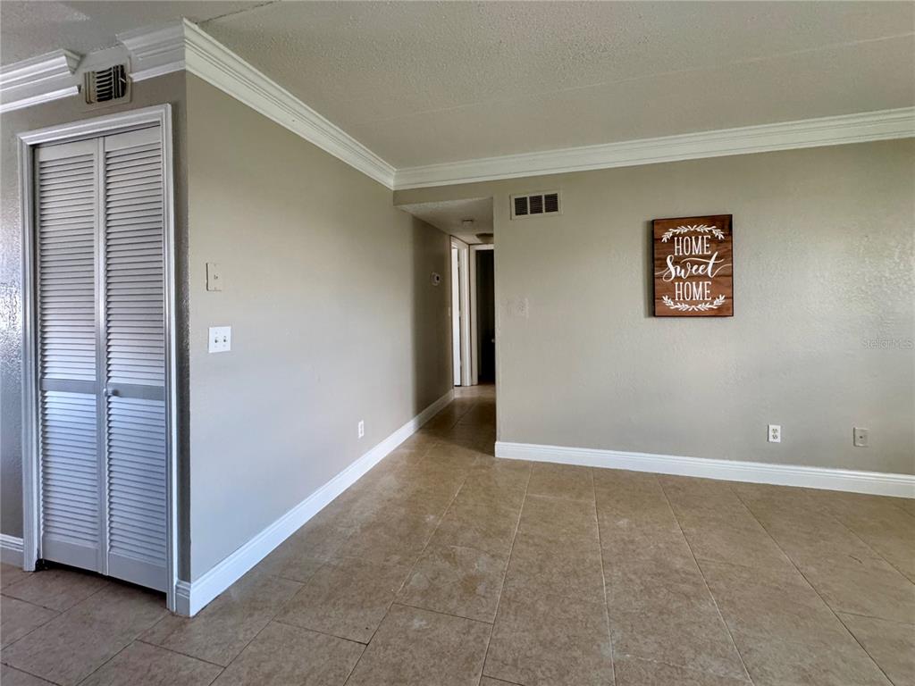 A room with beige walls, tile flooring, crown molding, and a louvered closet door — 1400 EUDORA ROAD UNIT D36, MOUNT DORA, FL
