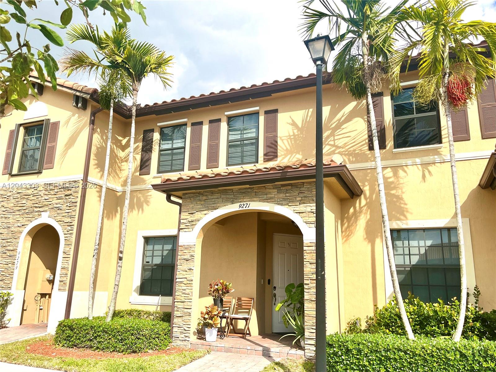 A two-story stucco townhouse features a stone-accented entryway, brown shutters, and palm trees — 9271 W 33rd Ln # 9271, Hialeah FL 33018, HIALEAH, FL