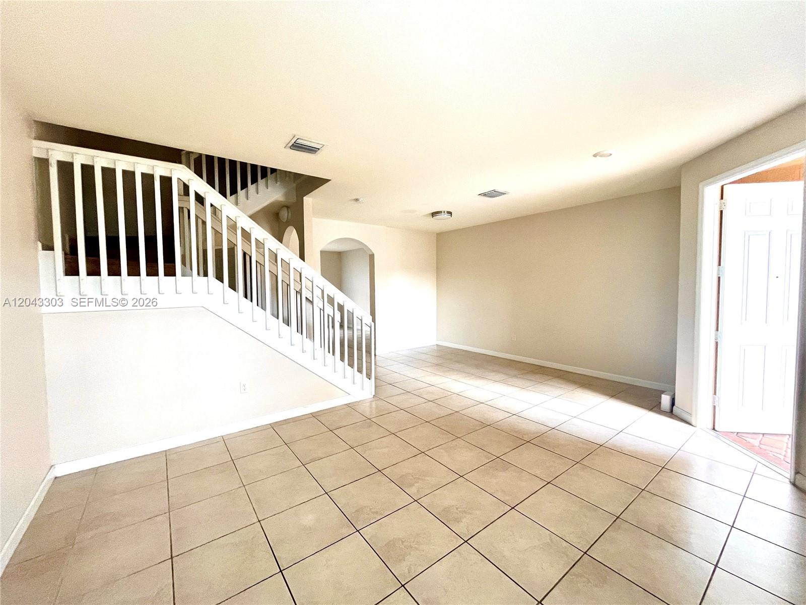 An empty room features beige tile flooring, a white staircase, and an open doorway — 9271 W 33rd Ln # 9271, Hialeah FL 33018, HIALEAH, FL