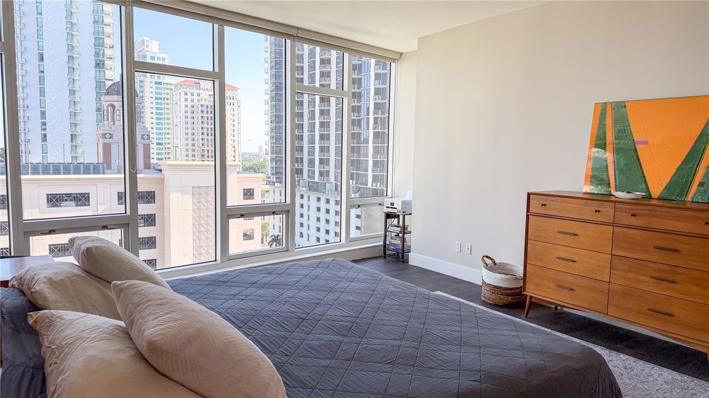 A bedroom features a dark quilt, a wooden dresser, and floor-to-ceiling windows overlooking city buildings — 175 1ST STREET S UNIT 1108, ST PETERSBURG, FL