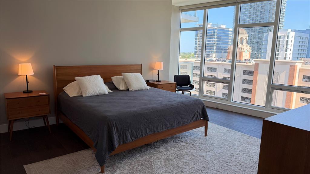 A bedroom features a wooden bed frame, two nightstands, and floor-to-ceiling windows overlooking city buildings — 175 1ST STREET S UNIT 1108, ST PETERSBURG, FL