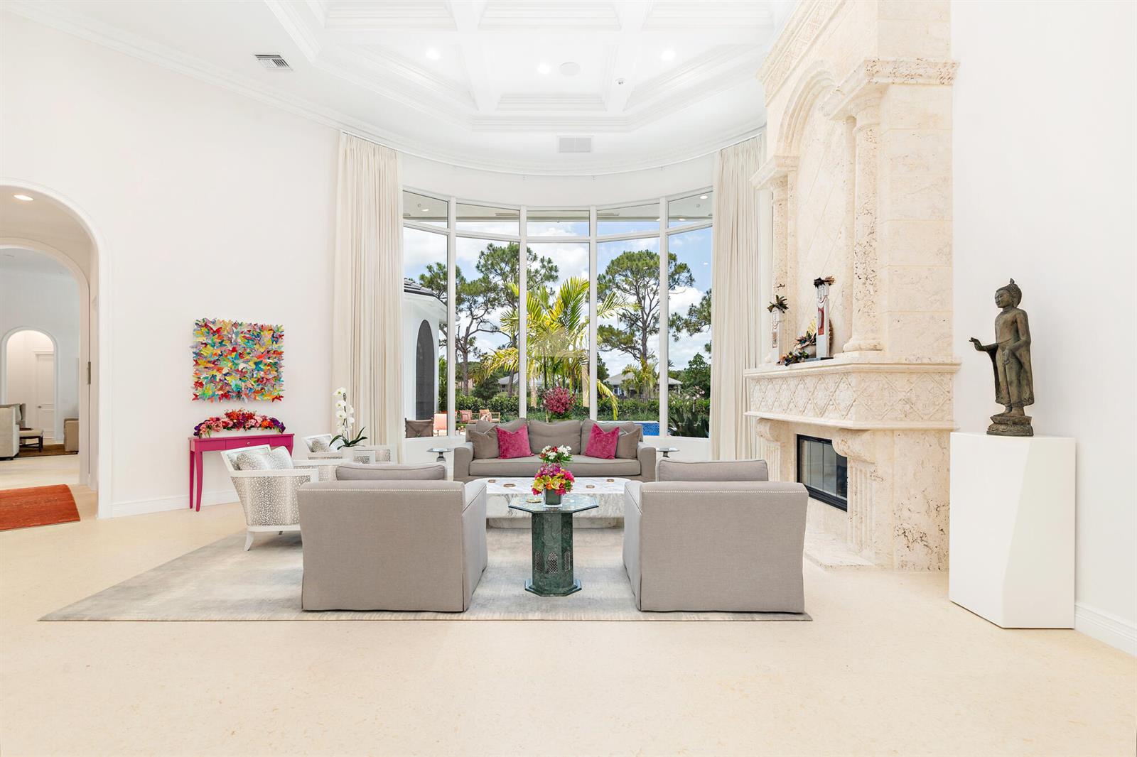 A bright living room features a large stone fireplace, floor-to-ceiling windows, and neutral furniture — 2707 Sheltingham Drive, Wellington FL 33414, WELLINGTON, FL