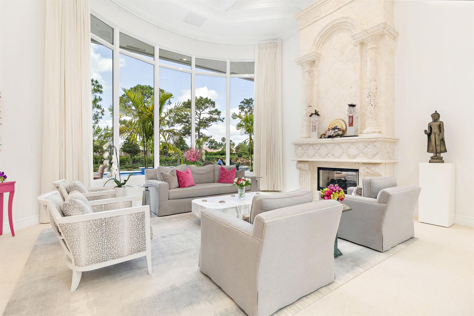 A bright living room features a large stone fireplace, floor-to-ceiling windows, and contemporary furniture — 2707 Sheltingham Drive, Wellington FL 33414, WELLINGTON, FL