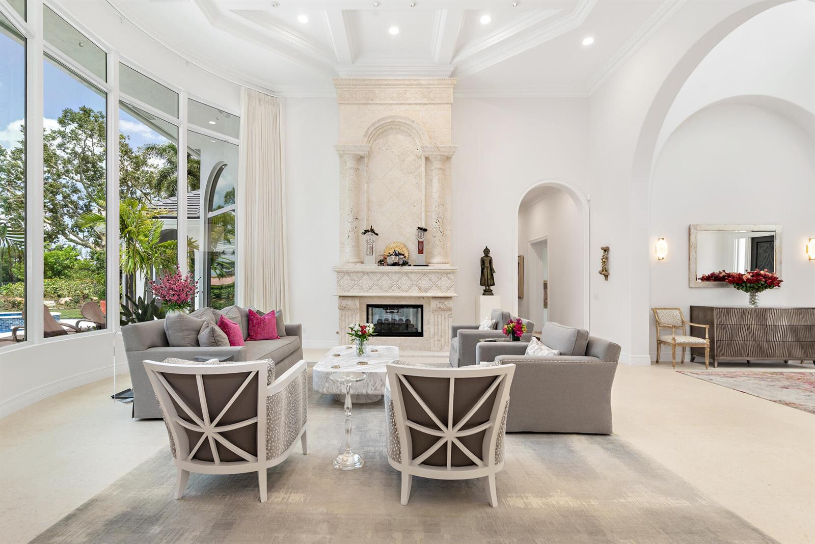 A bright, high-ceilinged living room features a large stone fireplace and floor-to-ceiling windows — 2707 Sheltingham Drive, Wellington FL 33414, WELLINGTON, FL