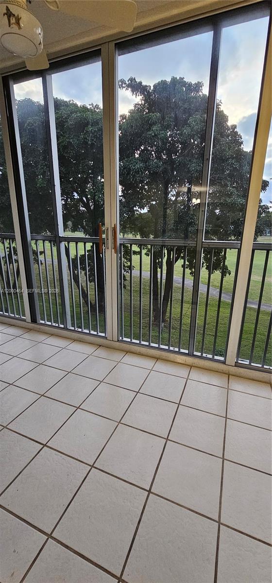 A tiled balcony features sliding glass doors overlooking a grassy area with mature trees — PEMBROKE PINES, FL