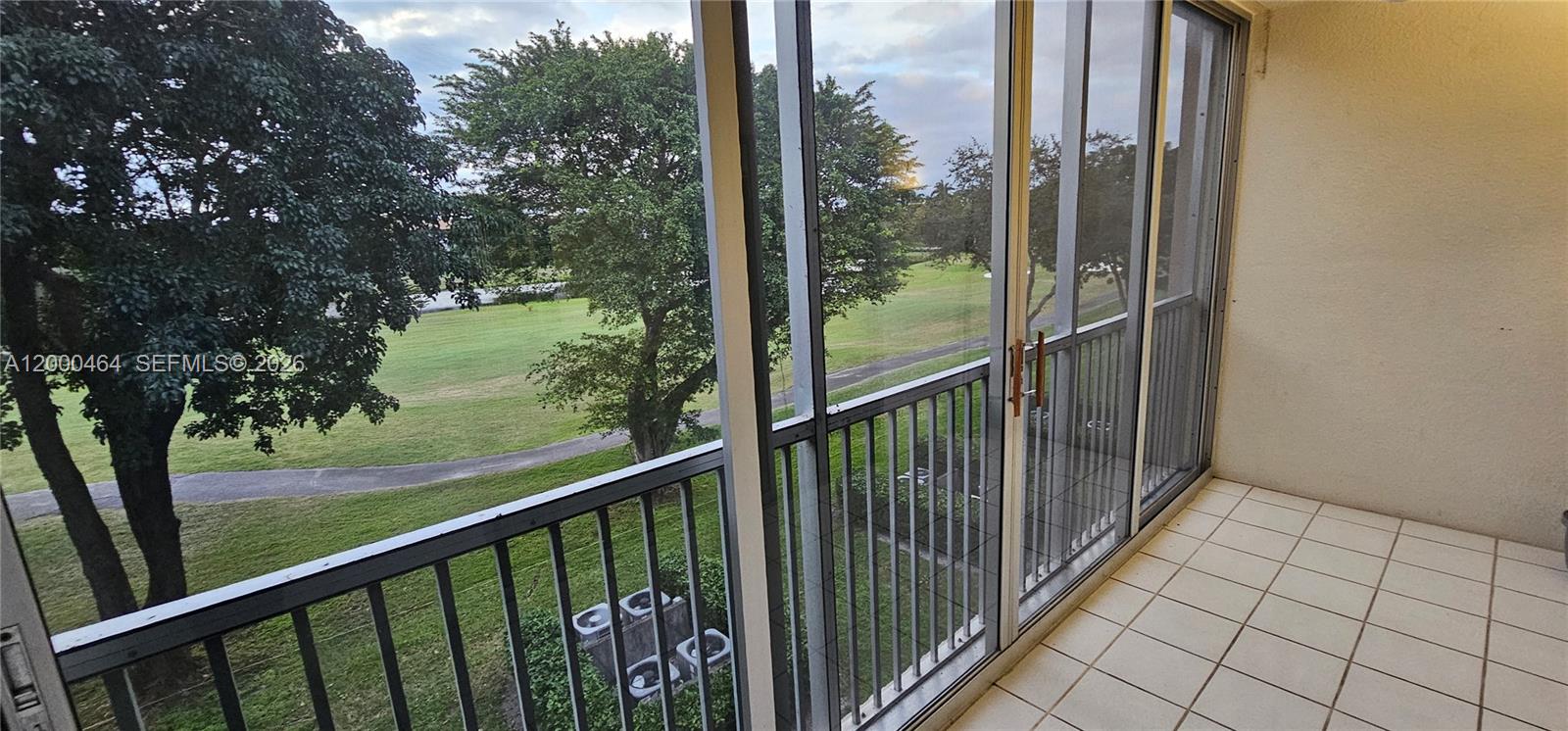 A tiled balcony features a metal railing and sliding glass doors overlooking a golf course — PEMBROKE PINES, FL